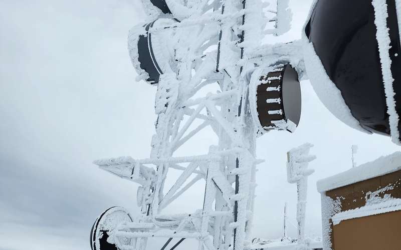A rime-iced lattice tower with microwave dishes at a mountaintop radio site after a winter storm, March 2024
