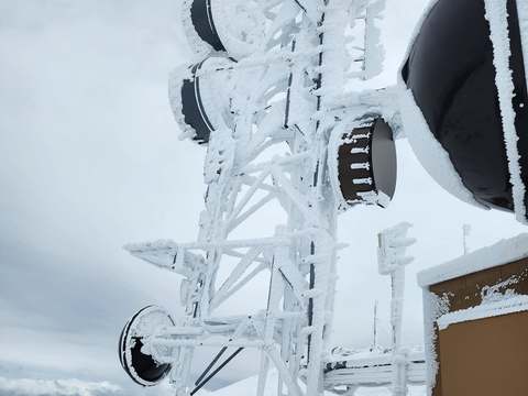 A rime-iced lattice tower with microwave dishes at a mountaintop radio site after a winter storm, March 2024
