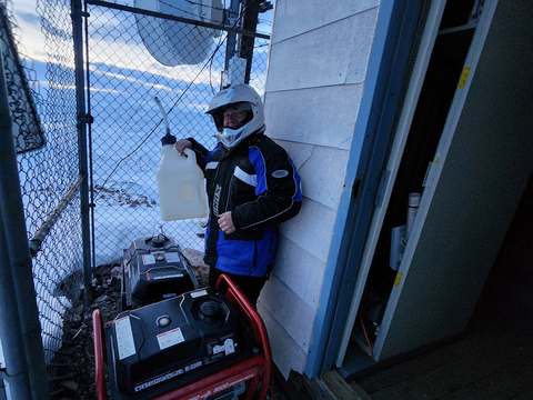 A technician in a helmet and winter gear refuelling a generator inside a fenced tower compound in the January 2023 storm